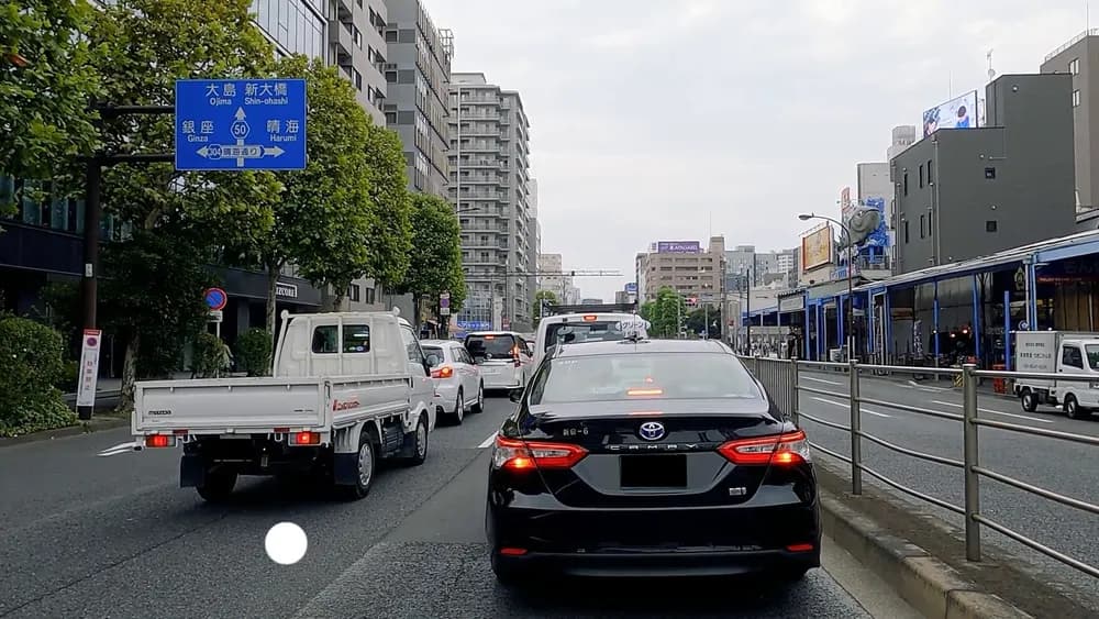 直進を示す上向き矢印の上に大島と新大橋、その下の段に銀座と晴海が並ぶ青い道路案内標識を、渋滞した市街地の車内から撮影した写真
