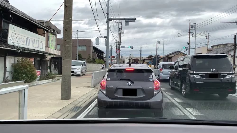 前方の信号が青にもかかわらず、すぐ前のコンパクトカーがブレーキランプを点灯させ、右側の車線にも車列が続いている車載カメラからの写真